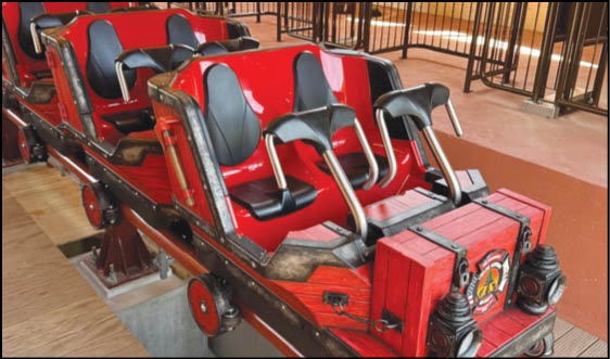A red roller coaster train with black seats is stationary on the track inside a loading area with metal railings. Description generated by AI