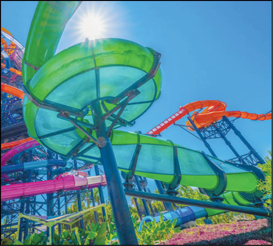 A colorful outdoor water park features multiple twisting and looping water slides in green, orange, pink, and blue under a bright sunny sky. Description generated by AI