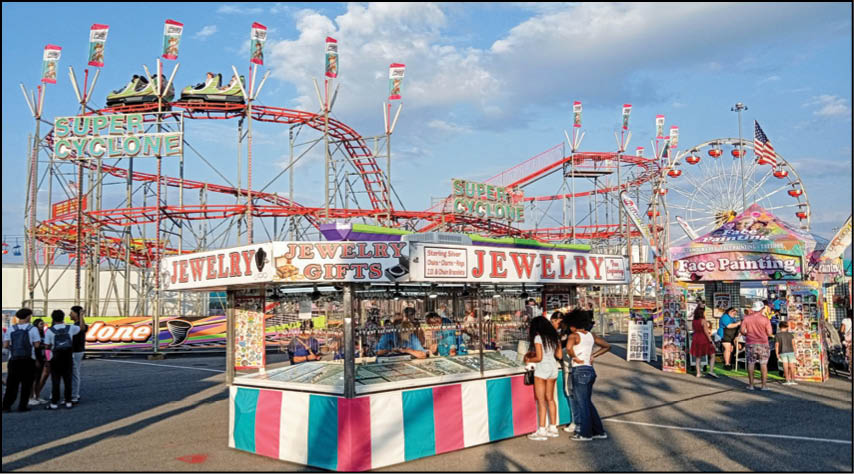 A colorful outdoor carnival scene with a roller coaster, a Ferris wheel, and booths selling jewelry and face painting with people walking and browsing. Description generated by AI