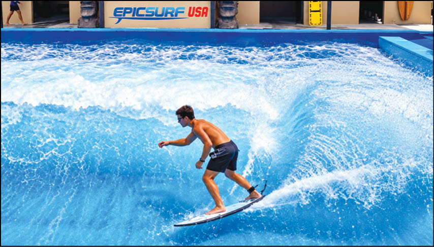A person wearing dark shorts is surfing on a wave in a pool with a sign that reads EPICSURF USA in the background. Description generated by AI