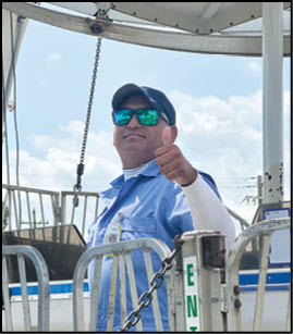 A person wearing a blue uniform, cap, and reflective sunglasses is giving a thumbs-up while standing behind a metal gate with a chain. Description generated by AI