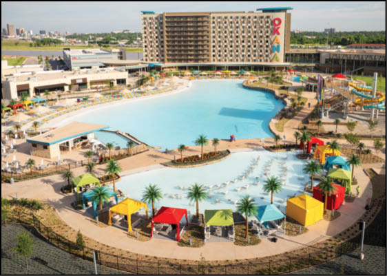 A large outdoor resort pool area with colorful cabanas, palm trees, lounge chairs, water slides, and a multi-story hotel building in the background. Description generated by AI