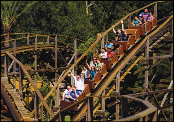 People riding a wooden roller coaster through a forested area with some raising their hands in excitement. Description generated by AI