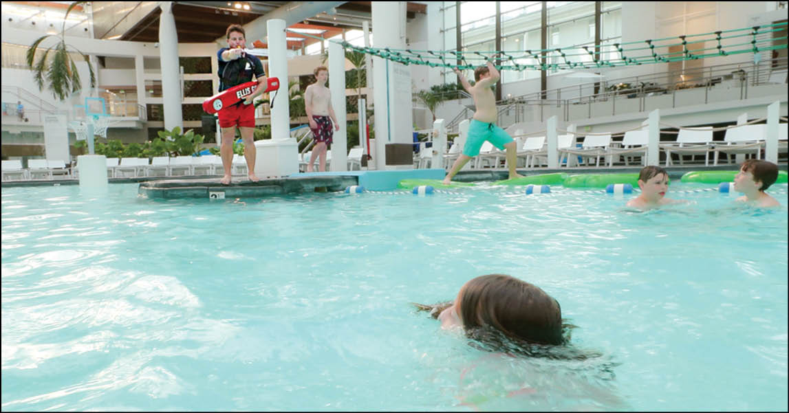 Children are playing and swimming in an indoor pool with one child holding a skateboard on the poolside. Description generated by AI