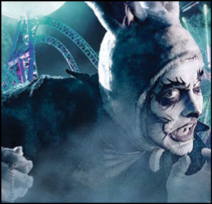 A person with dramatic face paint wearing a white rabbit costume is crouched in a foggy amusement park setting with roller coaster tracks in the background. Description generated by AI