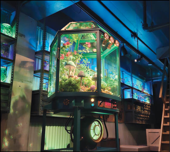 A futuristic glass terrarium filled with plants and mushrooms is displayed on a metal stand in a dimly lit room with blue ambient lighting and industrial shelving. Description generated by AI