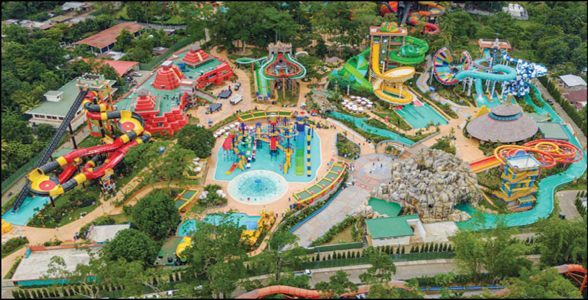 A colorful water park with multiple slides, pools, play structures, and surrounding greenery viewed from above. Description generated by AI