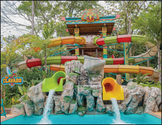 A colorful water park slide structure with multiple twisting tubes and two water slides pouring into a pool surrounded by rocks and greenery. Description generated by AI