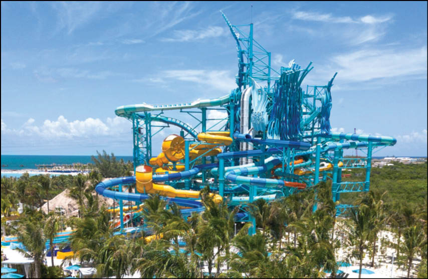 A large colorful water park with multiple twisting water slides surrounded by palm trees and a view of the ocean in the background. Description generated by AI