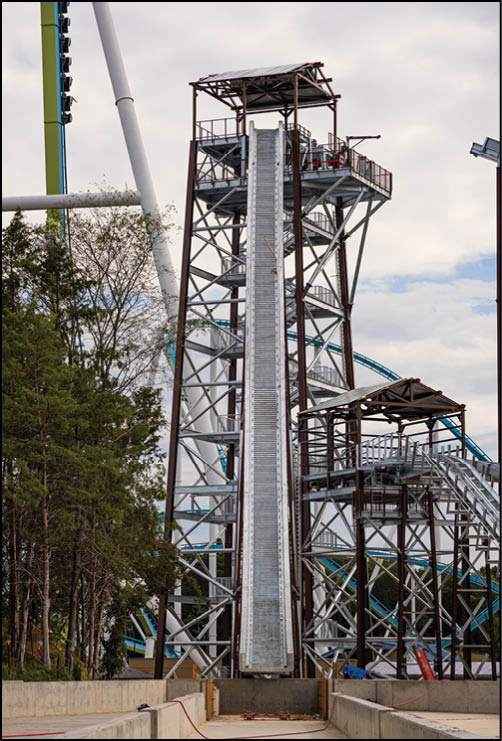 A group of people is seated in a vertical amusement park ride that is suspended between two large white support beams against a cloudy sky. Description generated by AI