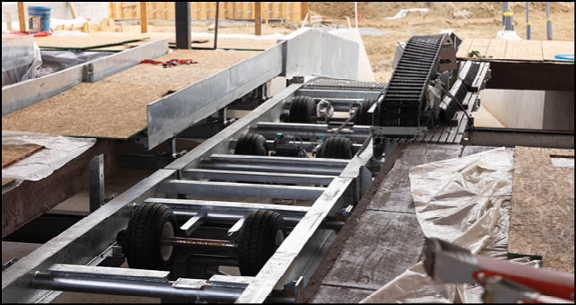 A close-up view of a metal frame structure with wheels, possibly part of a vehicle chassis, next to a wooden surface covered with a partially folded tarp. Description generated by AI