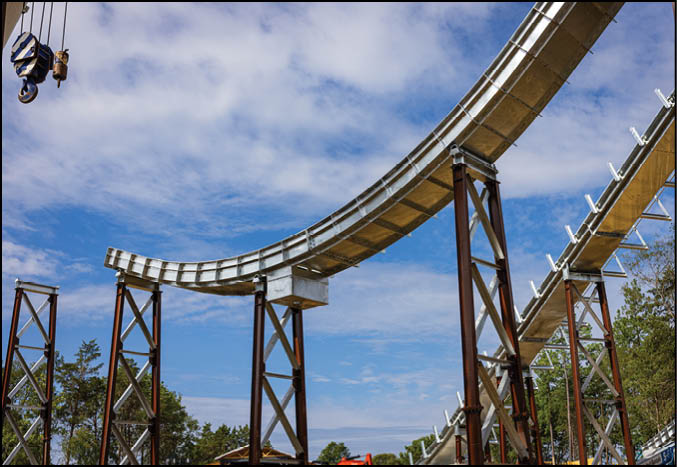 A section of an elevated roller coaster track supported by metal beams is shown against a partly cloudy blue sky. Description generated by AI
