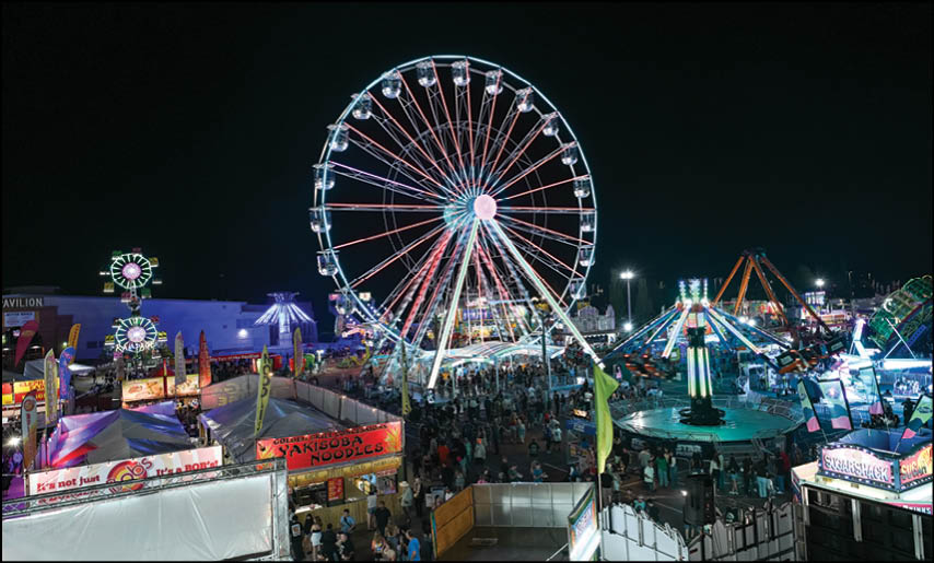 A brightly lit Ferris wheel and various amusement rides illuminate a crowded nighttime carnival scene. Description generated by AI