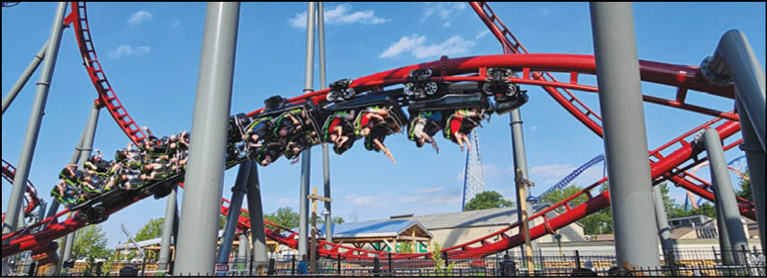 A group of people are riding a red roller coaster that is twisting and turning outdoors on a sunny day. Description generated by AI