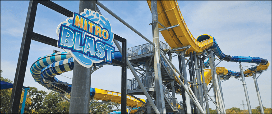 A colorful water slide structure with twisting yellow and blue tubes is set against a clear blue sky with a sign that reads Nitro Blast. Description generated by AI