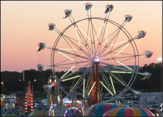 A brightly lit Ferris wheel stands against a sunset sky at a lively carnival with colorful tents and other illuminated rides. Description generated by AI