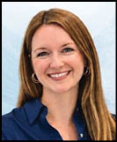 A person with long straight hair wearing a dark blue collared shirt is smiling against a light blue background. Description generated by AI