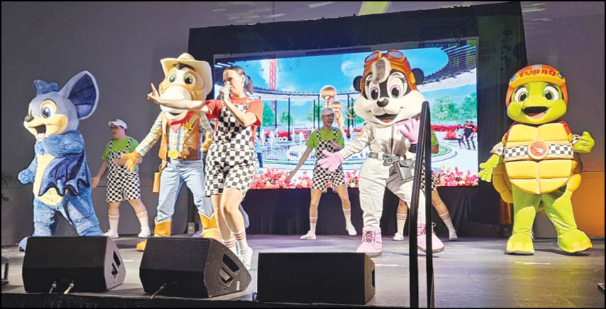 People in colorful costumes and checkered outfits are performing on a stage with a large screen in the background. Description generated by AI