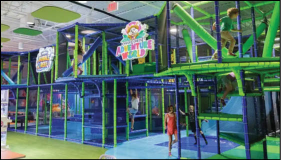 Children are playing and climbing inside a colorful indoor playground structure labeled “Adventure World" with green and blue padded bars and platforms. Description generated by AI