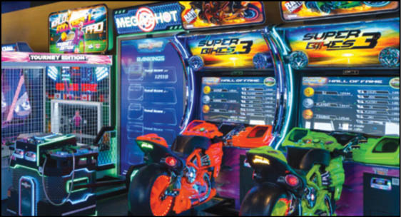 Two brightly colored arcade motorcycle racing games with neon lights are positioned side by side in a gaming arcade. Description generated by AI