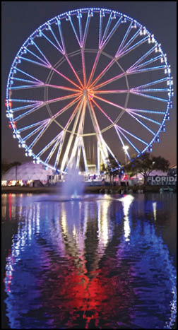 A large blue and white Ferris wheel with a red reflection in the water. Description generated by AI