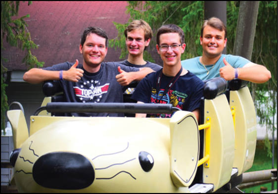 A group of four people are riding a yellow and black merry go round. Description generated by AI