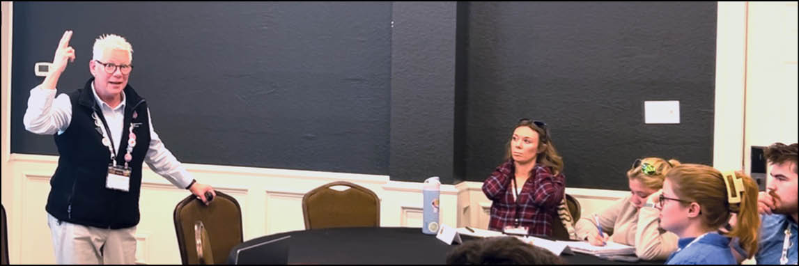 A man is standing in front of a group of people. Description generated by AI