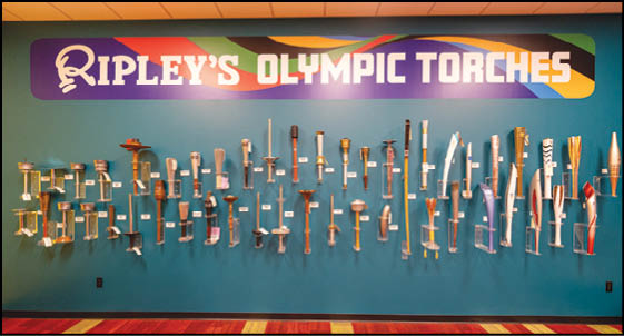 A wall with a blue background and a row of Olympic torches. Description generated by AI