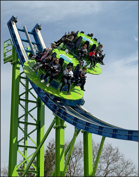 A green and blue roller coaster with people riding it. Description generated by AI