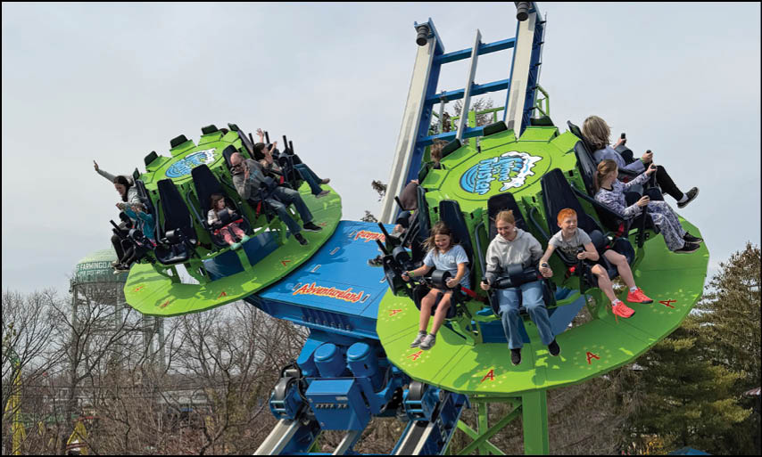 A green and blue roller coaster with people riding it. Description generated by AI