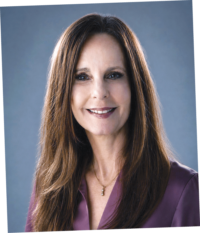 A woman with long brown hair and a purple shirt. Description generated by AI