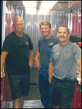 Three men standing in a red and white room. Description generated by AI