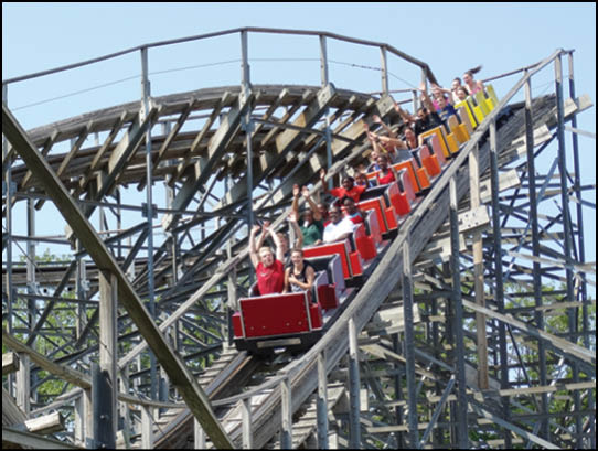 A wooden roller coaster with people riding it. Description generated by AI