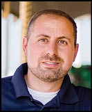 A man is smiling in front of a merry go round. Description generated by AI