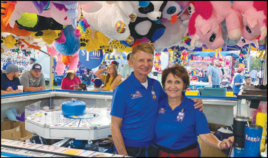 A man and woman standing in a carnival booth. Description generated by AI