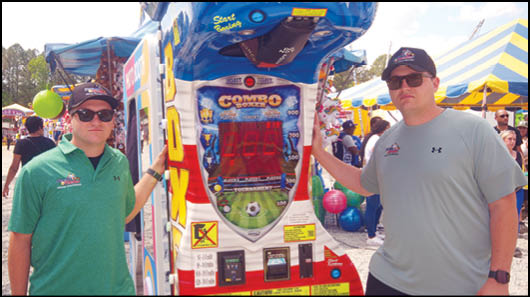 Two men standing in front of a video game machine. Description generated by AI