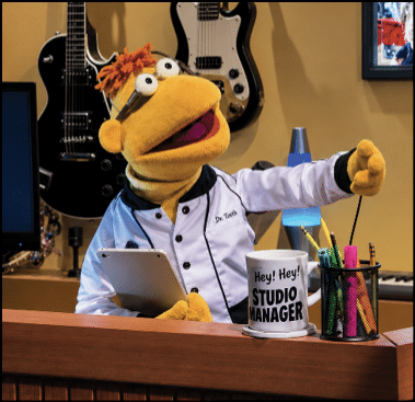 A puppet in a white shirt and apron sitting at a desk. Description generated by AI