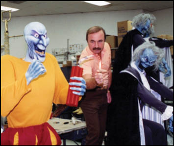 A man standing in front of a group of Halloween costumes. Description generated by AI