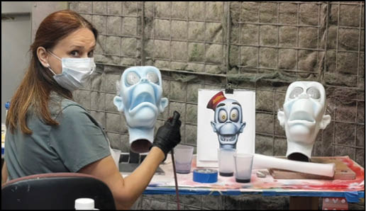 A woman wearing a mask is painting a sculpture of a face. Description generated by AI