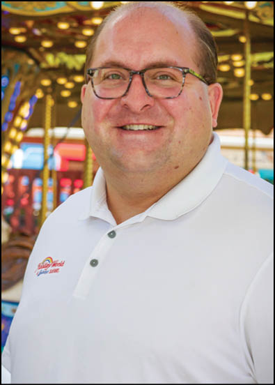 A man wearing a white shirt with a logo on it. Description generated by AI