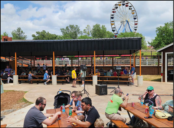 People sitting at picnic tables under a large black umbrella. Description generated by AI