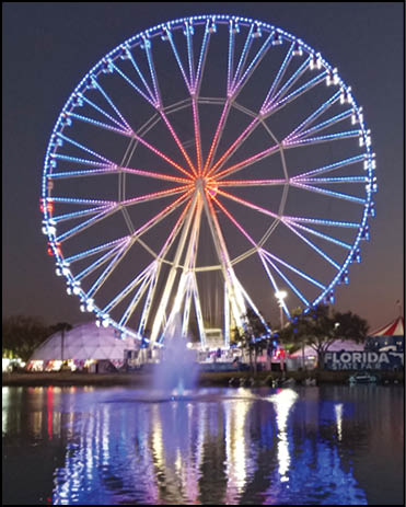A large blue and white Ferris wheel with a red reflection in the water. Description generated by AI