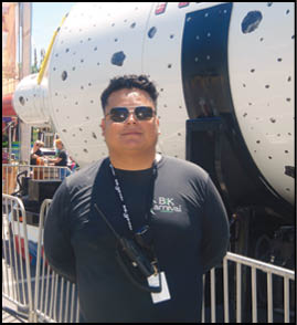 Two men standing in front of a carnival sign. Description generated by AI