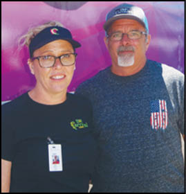 Two men standing in front of a carnival sign. Description generated by AI