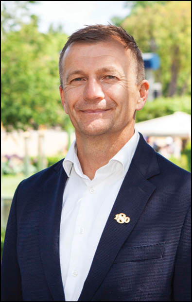 A man wearing a white shirt with a logo on it. Description generated by AI