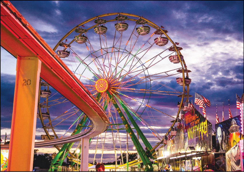 Two men standing in front of a carnival sign. Description generated by AI