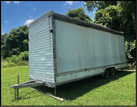 A clear blue sky with scattered white clouds is visible above the top corner of a white truck and green leafy trees. Description generated by AI