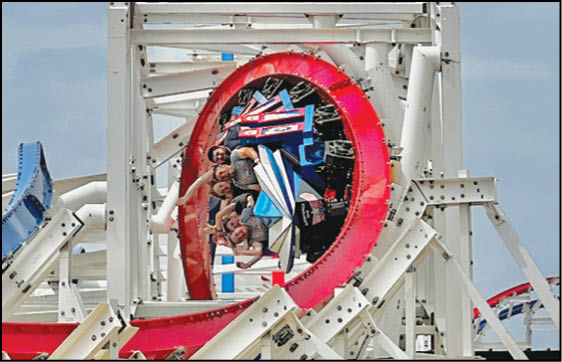 Four people are riding a roller coaster car that is upside down on a red circular loop against a clear sky background. Description generated by AI