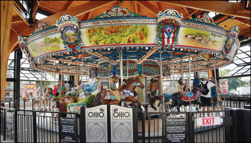 Two men standing in front of a carnival sign. Description generated by AI