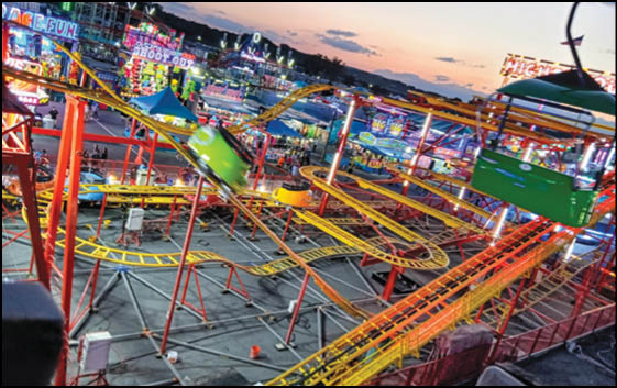 A colorful amusement park at dusk features a roller coaster with yellow tracks and green cars, surrounded by bright lights and various rides. Description generated by AI